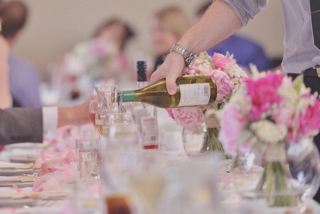 Garçom servindo vinho numa mesa de casamento decorada com flores cor-de-rosa